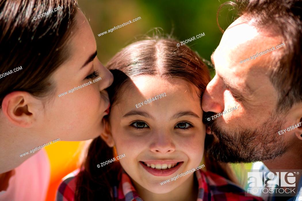 Stock Photo: Happy Patents Kissing Daughter Cheecks In Summer Park. Spending Time Together. Happy Family Concept.