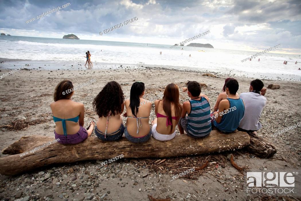 Stock Photo: Group of young people sitting on a log at the public beach of Manuel Antonio. Manuel Antonio National Park, Puntarenas, Pacific Ocean, Costa Rica.