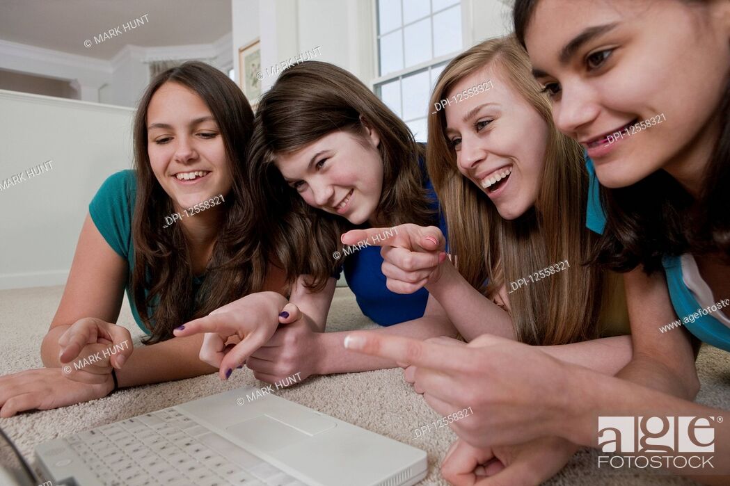 Stock Photo: Four teenage girls using a laptop and pointing at the screen while laughing.