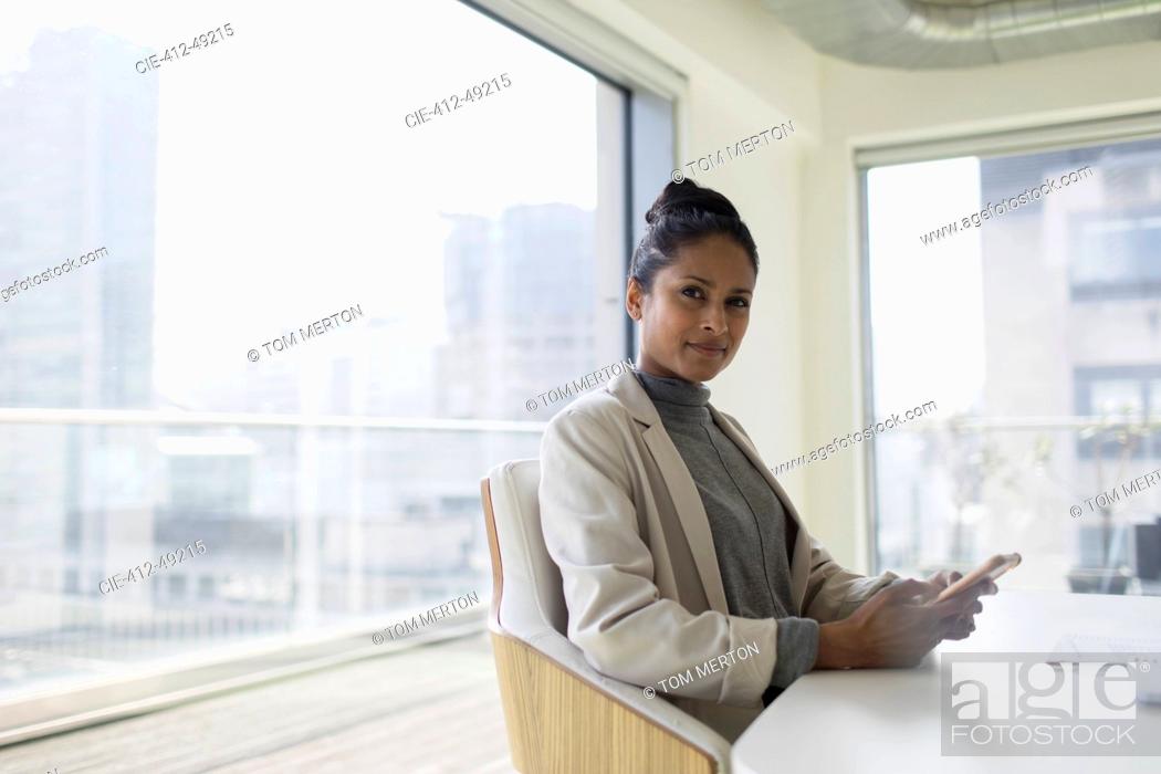 Stock Photo: Portrait confident businesswoman using smart phone in urban conference room.