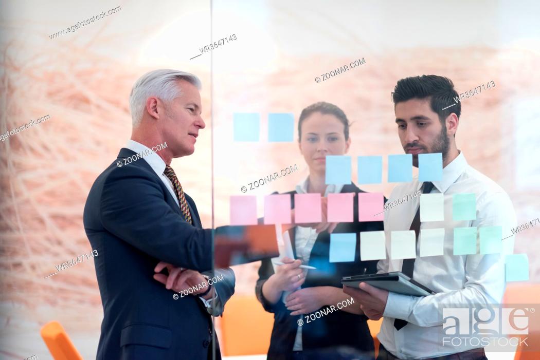Stock Photo: young creative startup business people on meeting with older senior mature businessman at modern office making plans and projects with post stickers on glass.