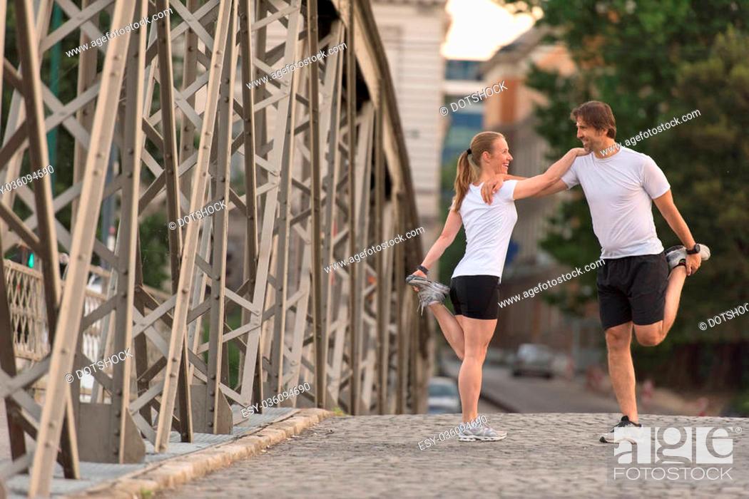 Stock Photo: jogging couple warming up and stretching before morning running training workout in the city with sunrise in background.