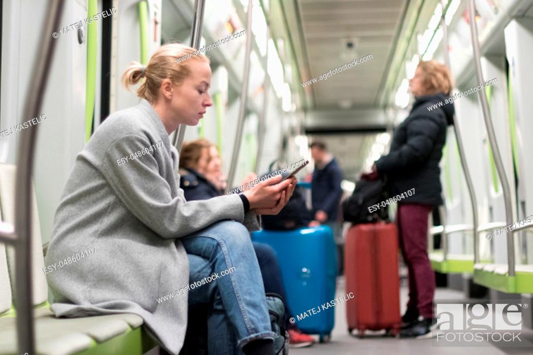 Stock Photo: Beautiful blonde caucasian woman wearing winter coat reading on the phone while traveling by metro. Public transportation concept.