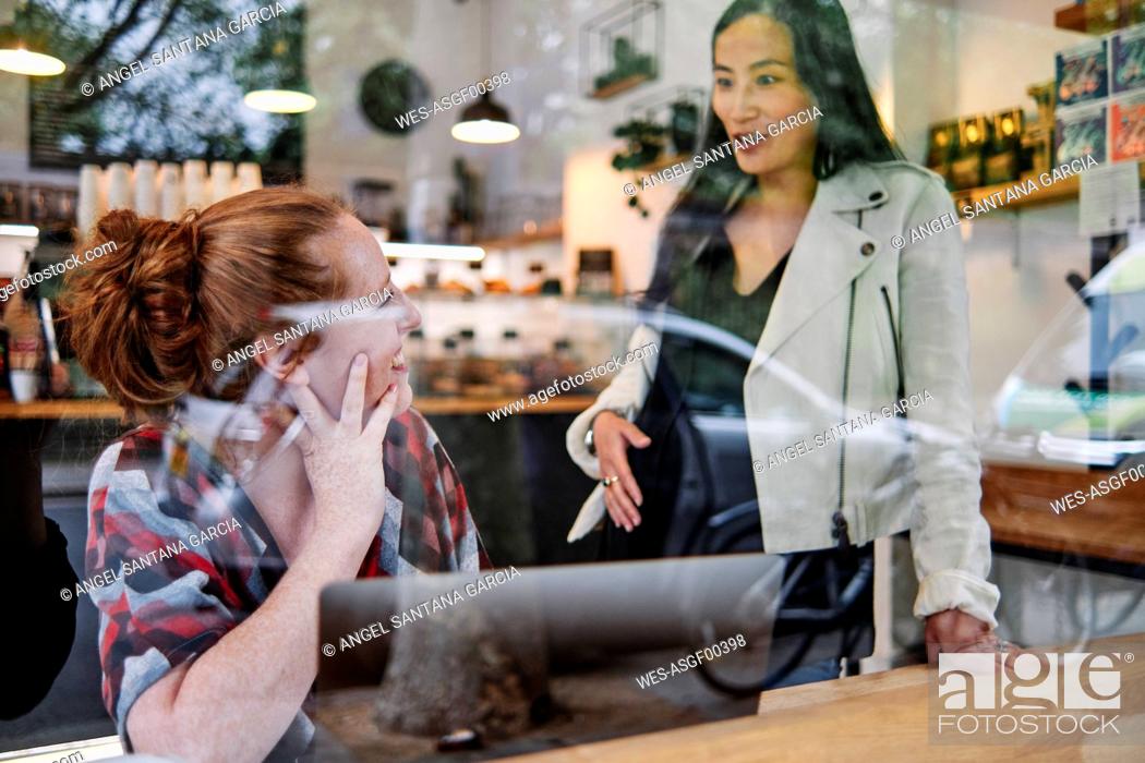 Stock Photo: Pregnant woman with hand on stomach talking with female friend in cafe.