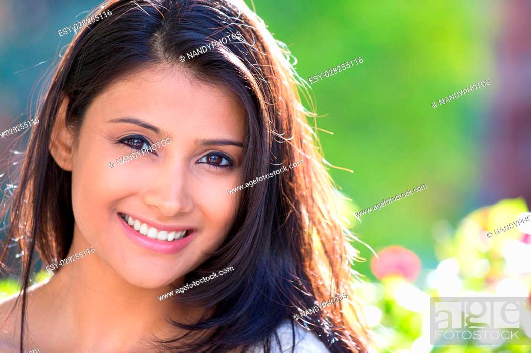 Stock Photo: Closeup headshot portrait of confident smiling happy pretty young woman, isolated background of blurred trees, flowers. Positive human emotion facial expression.