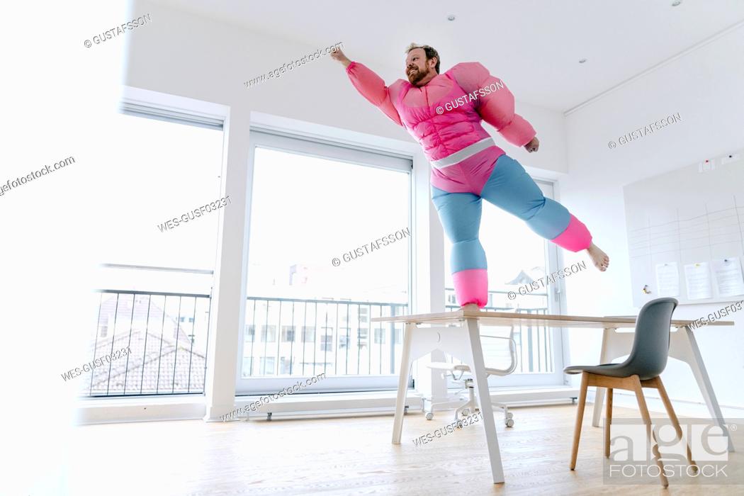 Stock Photo: Businessman in office wearing pink bodybuilder costume pretending to fly.