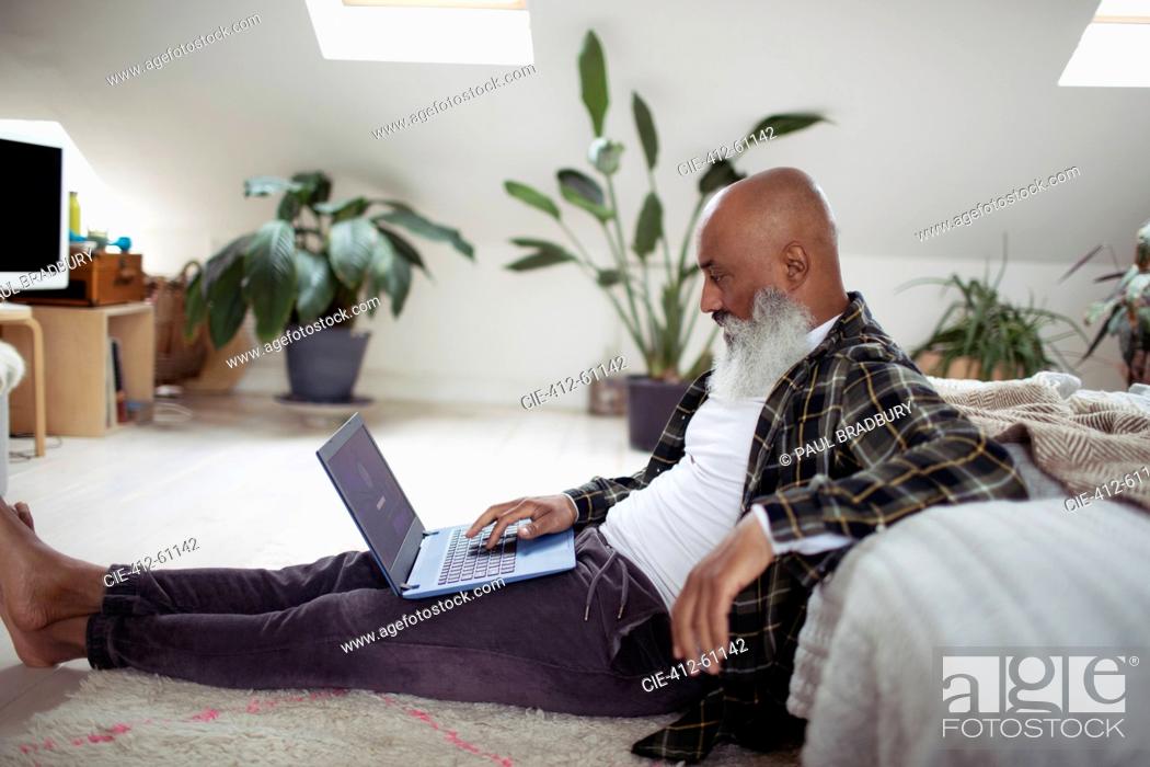 Stock Photo: Mature man with beard using laptop on bedroom floor.