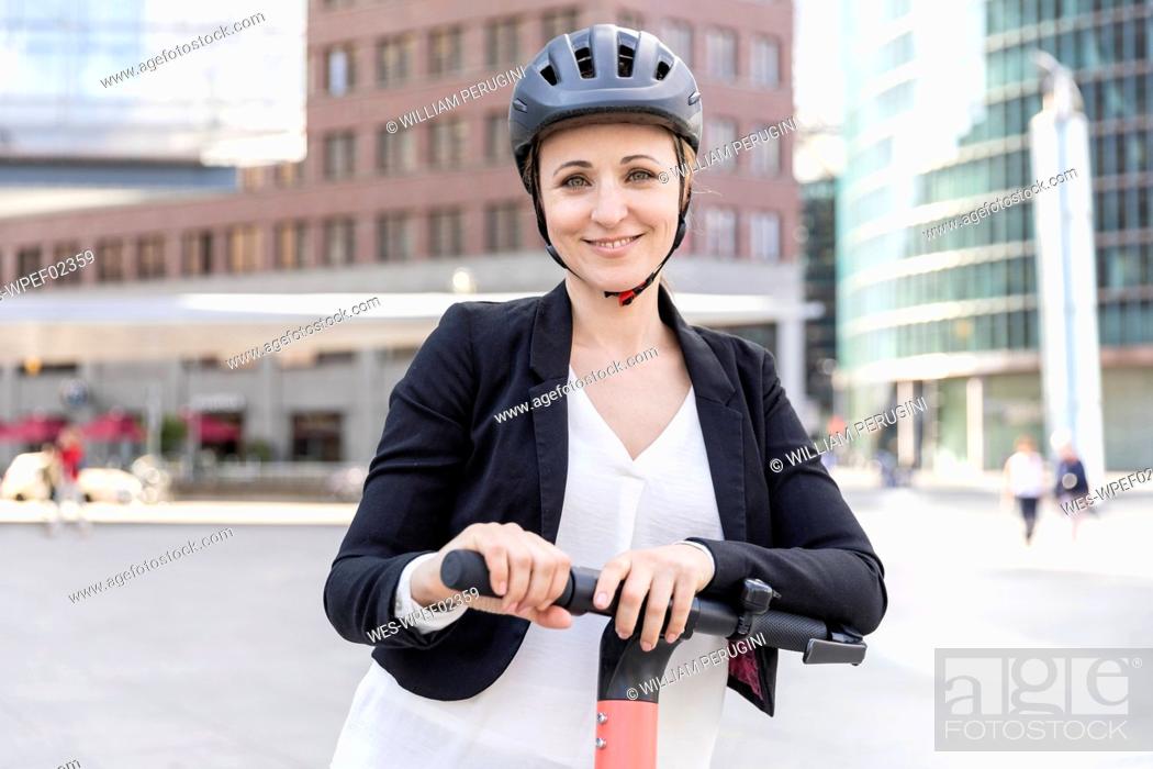 Stock Photo: Portrait of smiling woman with e-scooter in the city, Berlin, Germany.