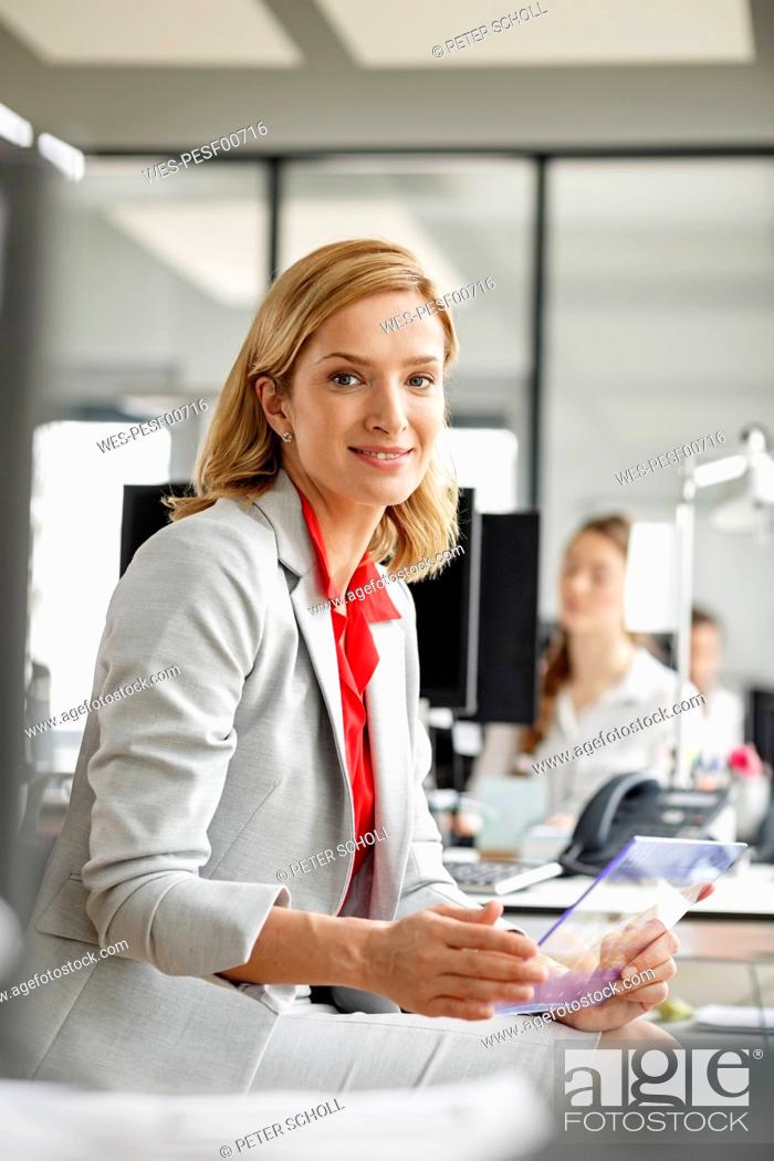 Stock Photo: Portait of smiling businesswoman at desk in office holding futuristic tablet.