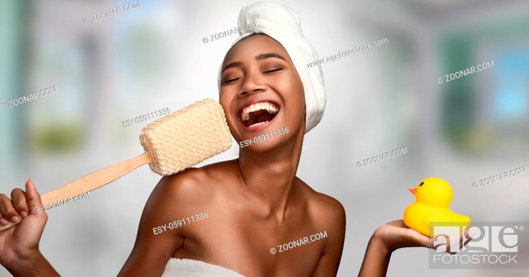 Stock Photo: Close-up portrait of a beautiful smiling happy woman holding body scrubber and yellow rubber duck isolated on bright background.