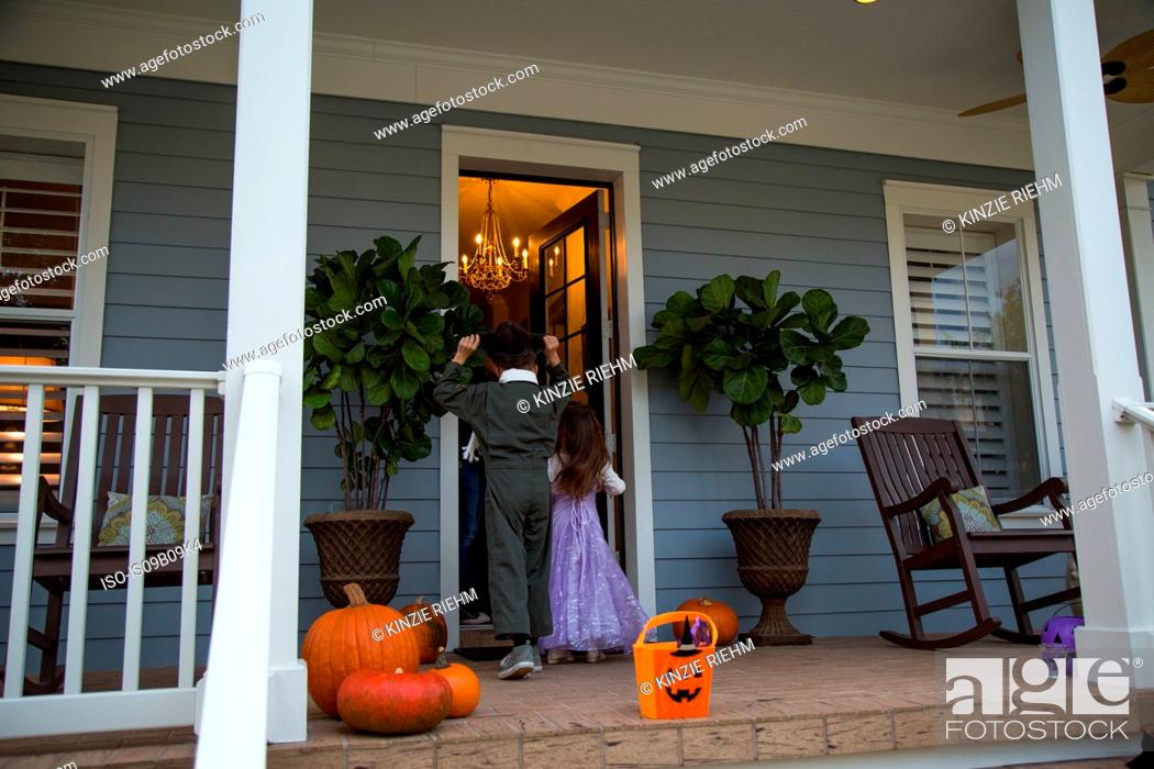 Stock Photo: Brother and sister trick or treating at neighbour's front door.