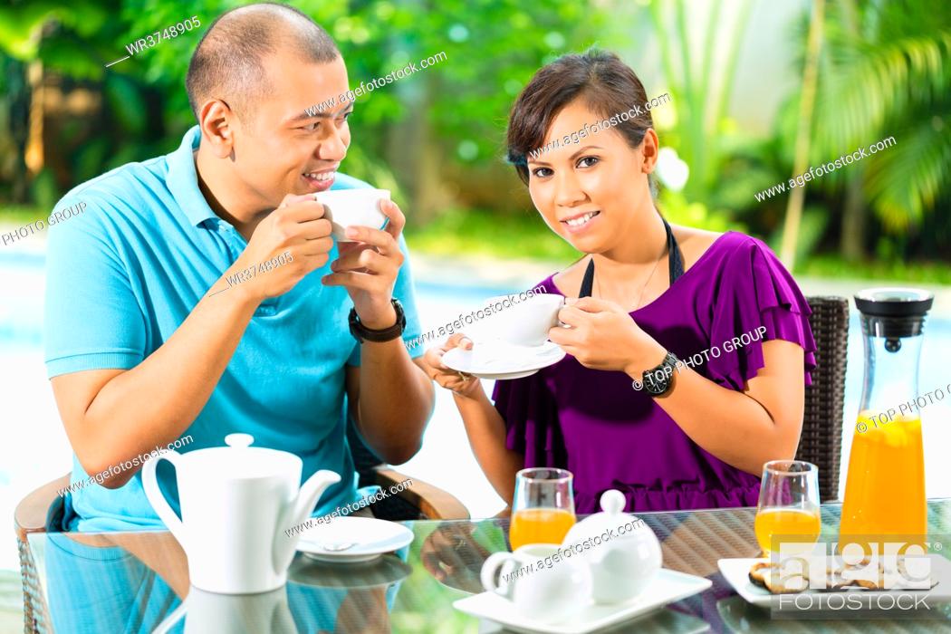 Photo de stock: Asian couple having coffee on the porch in front of their home, in the background a tropical garden.