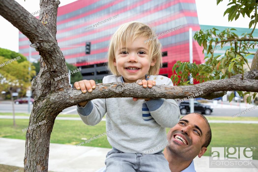 Stock Photo: Hispanic father and son playing on tree in park.