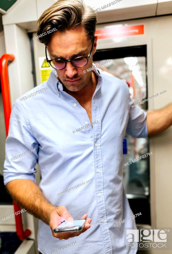 Stock Photo: UK, London, businessman in underground train looking at cell phone.