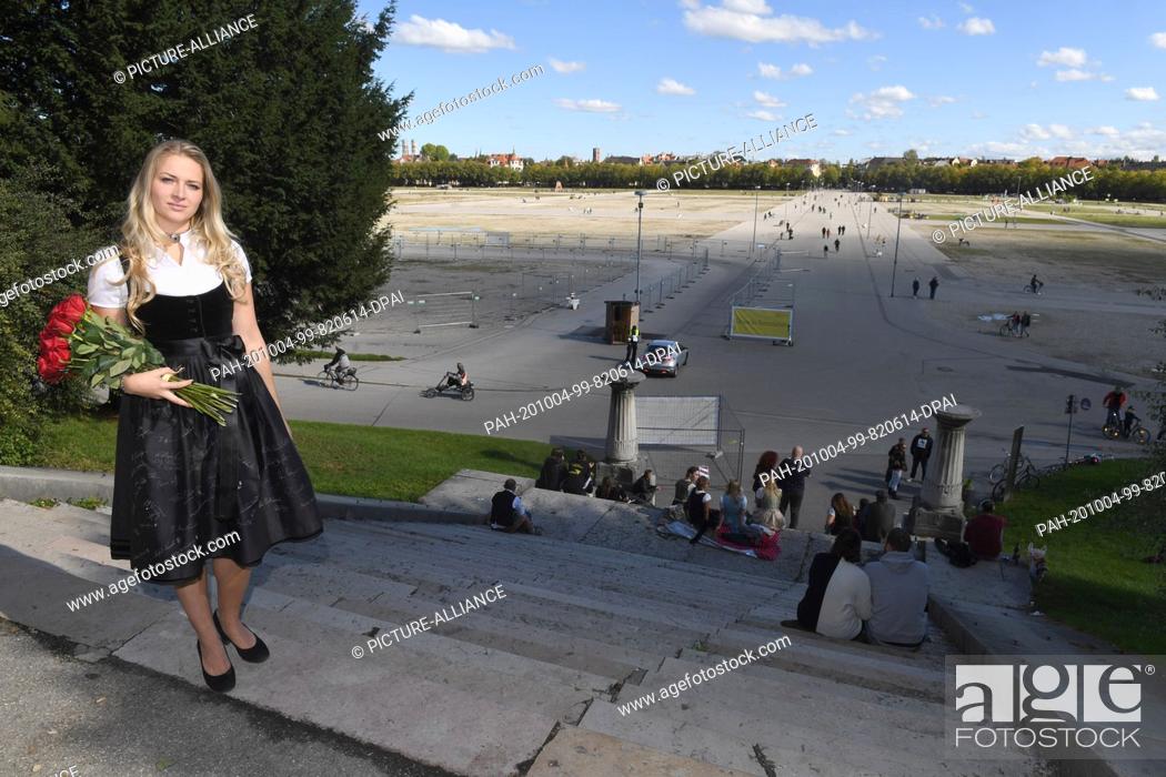 Stock Photo: 04 October 2020, Bavaria, Munich: The Munich child Viktoria Ostler stands in a black commemorative dirndl for the cancelled Wiesn 2020 with a bouquet of red.