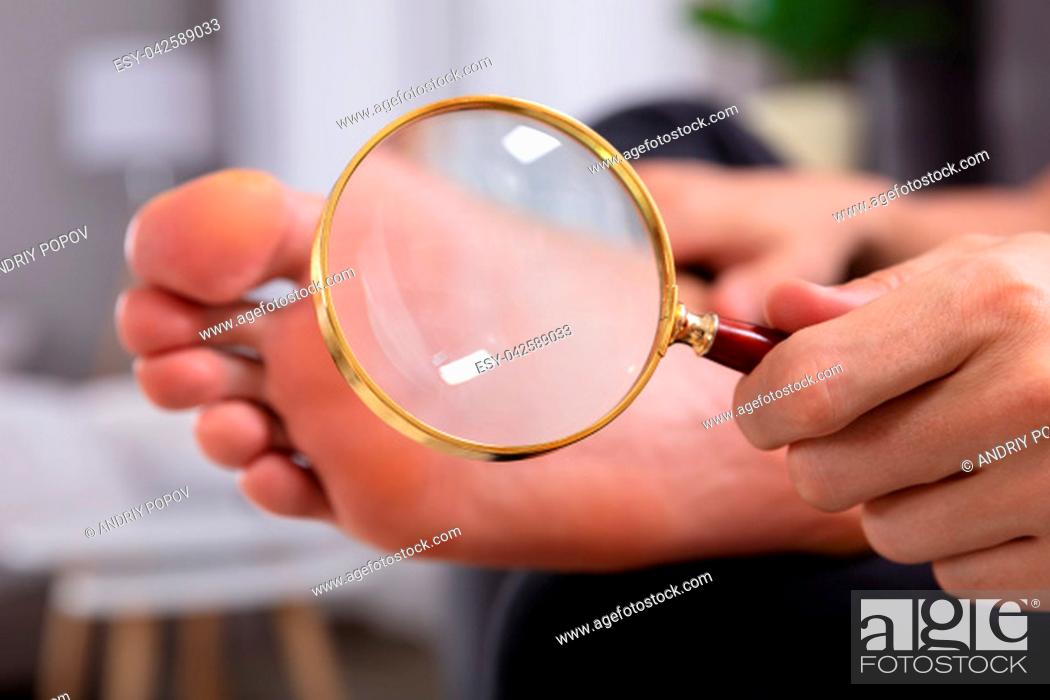 Stock Photo: Close-up Of A Man's Hand Holding Magnifying Glass In Front Of His Feet.