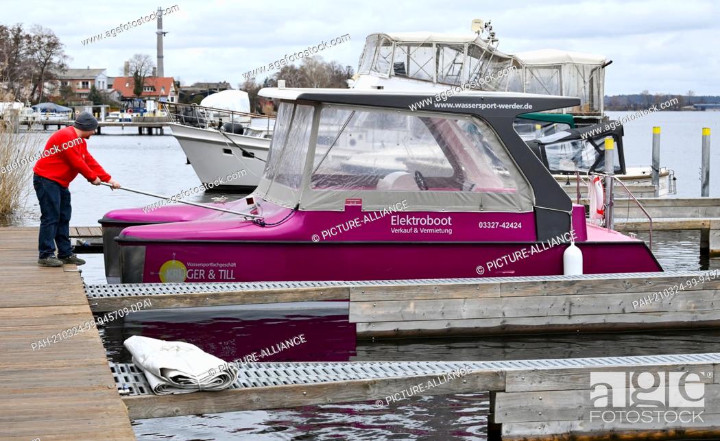 Stock Photo: 23 March 2021, Brandenburg, Werder (Havel): Kai Grunow from the water sports shop Krüger and Till secures an electric boat in the harbour of Werder.