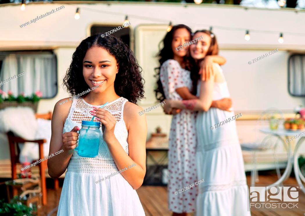 Stock Photo: Beautiful african american female portrait during picnic beside her camper van and friends on background. Vacation, trip and holiday concept.