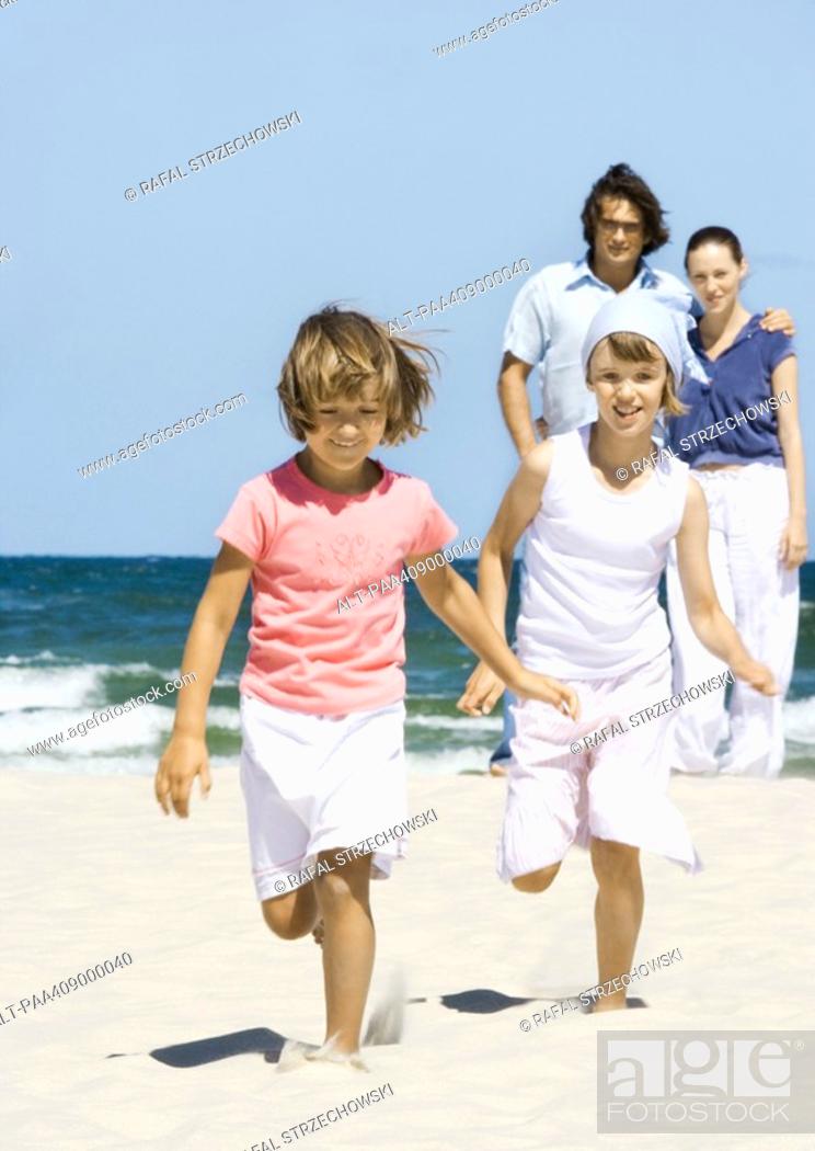 Imagen: Girls running on beach while parents stand in background.