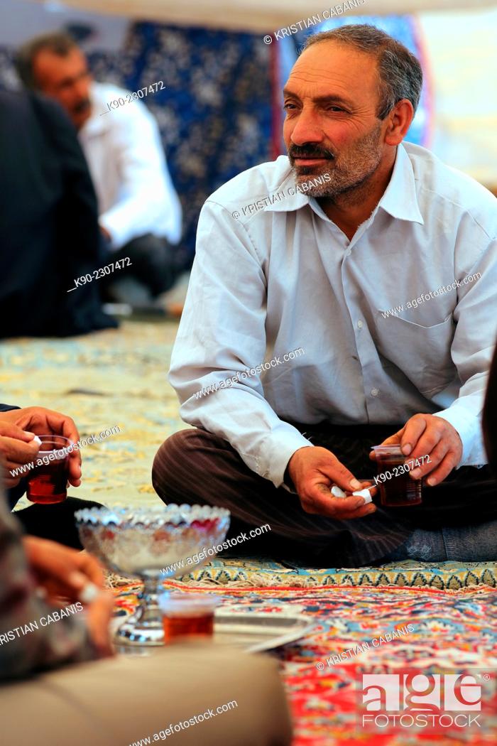 Photo de stock: Nomadic man sitting on a carpet during a wedding ceremony holding a cup of tea, Zagros mountains, Central Iran, Asia.