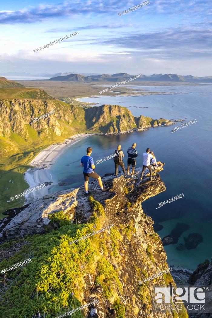 Stock Photo: Four hikers standing on rocky outcrop, view of rocks, beach and sea, summit of Måtinden mountain, near Stave, Nordland, Norway, Europe.