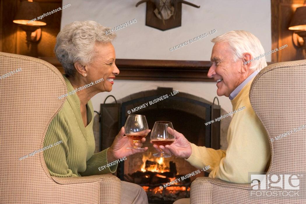 Stock Photo: Couple sitting in living room by fireplace with drinks smiling.