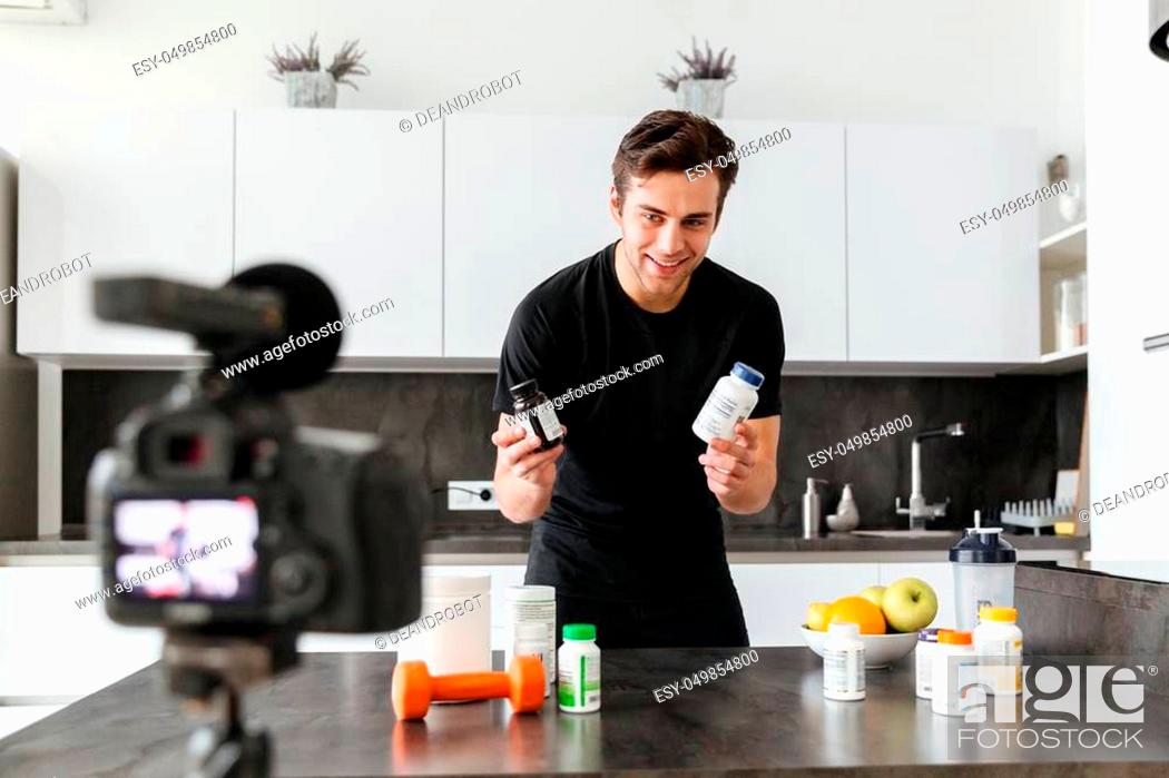 Stock Photo: Excited young man filming his video blog episode about healthy food additives while standing at the kitchen table.