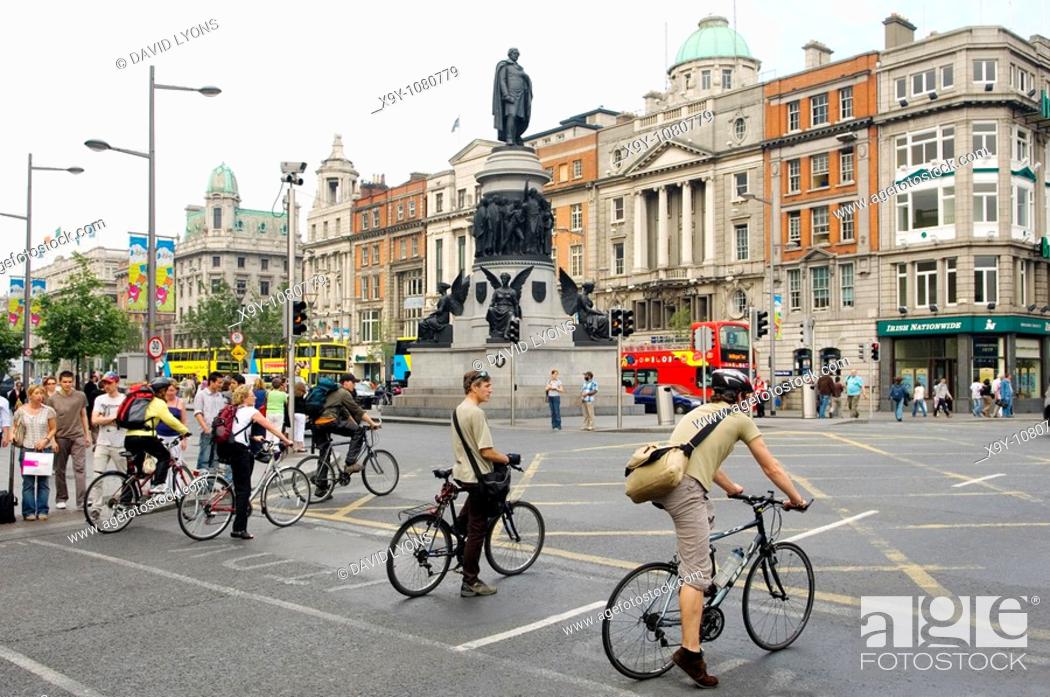 Stock Photo: Dublin City  Statue of Daniel O’Connell and cyclists waiting to cross O'Connell Street, the city centre main thoroughfare.