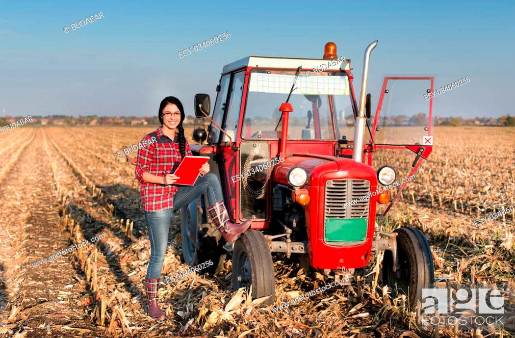 Stock Photo: Young farmer girl standing beside tractor in harvested corn field.