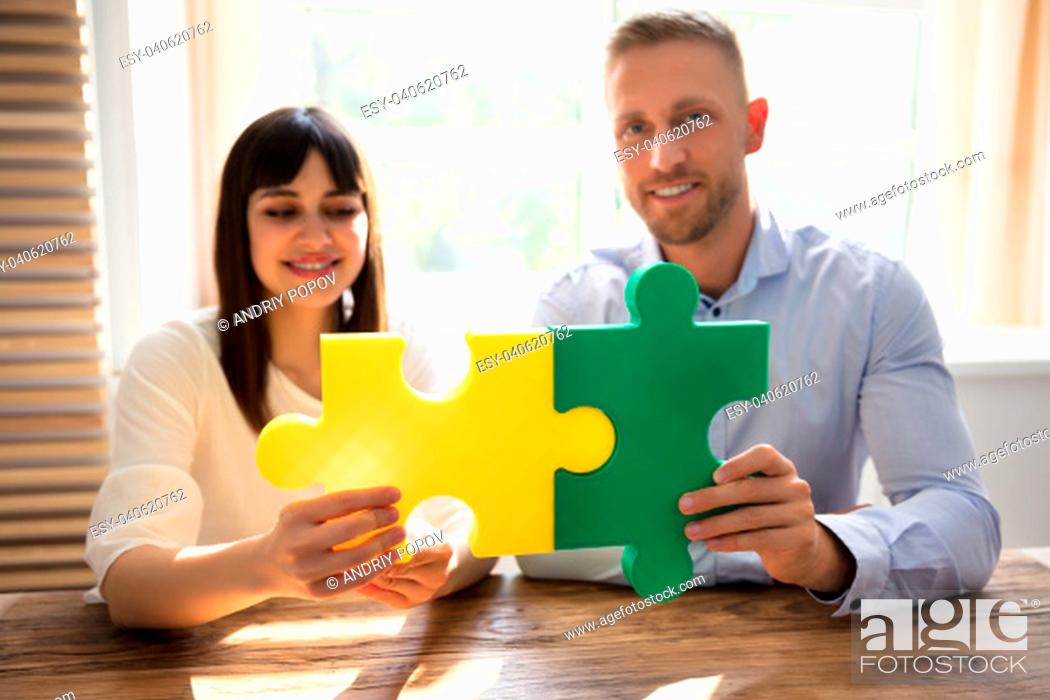 Stock Photo: Two Happy Businesspeople Joining Green And Yellow Colored Jigsaw Pieces.