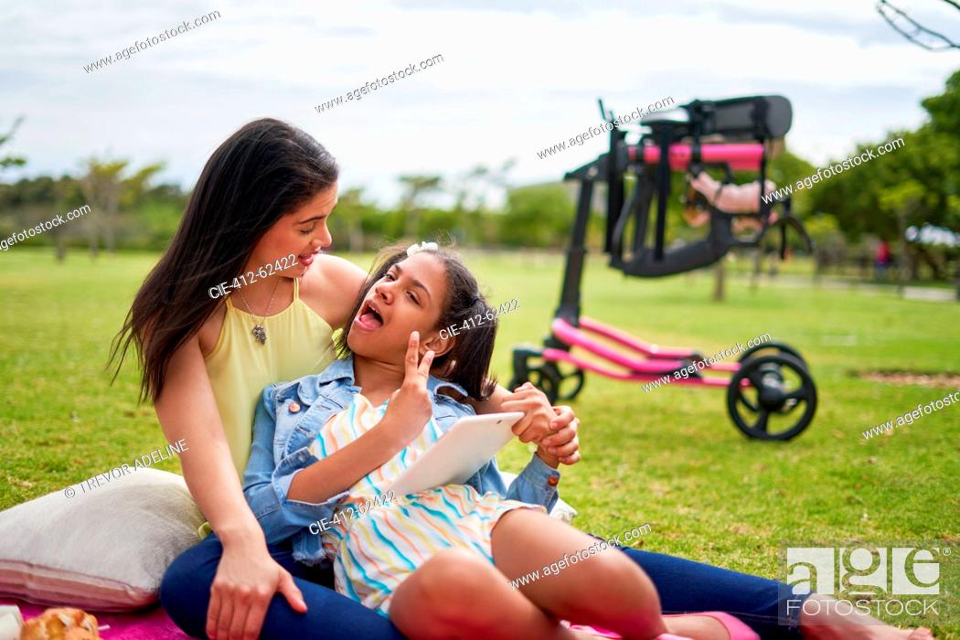 Imagen: Mother and disabled daughter with digital tablet on blanket in park.