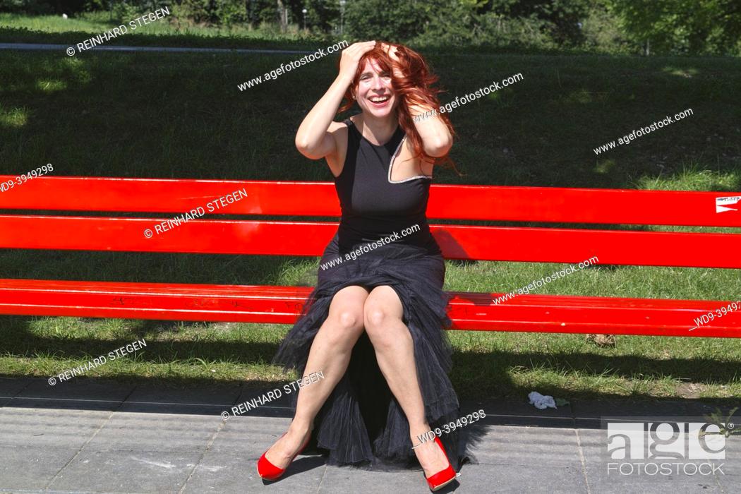 Photo de stock: young woman in black on red bench having fun.