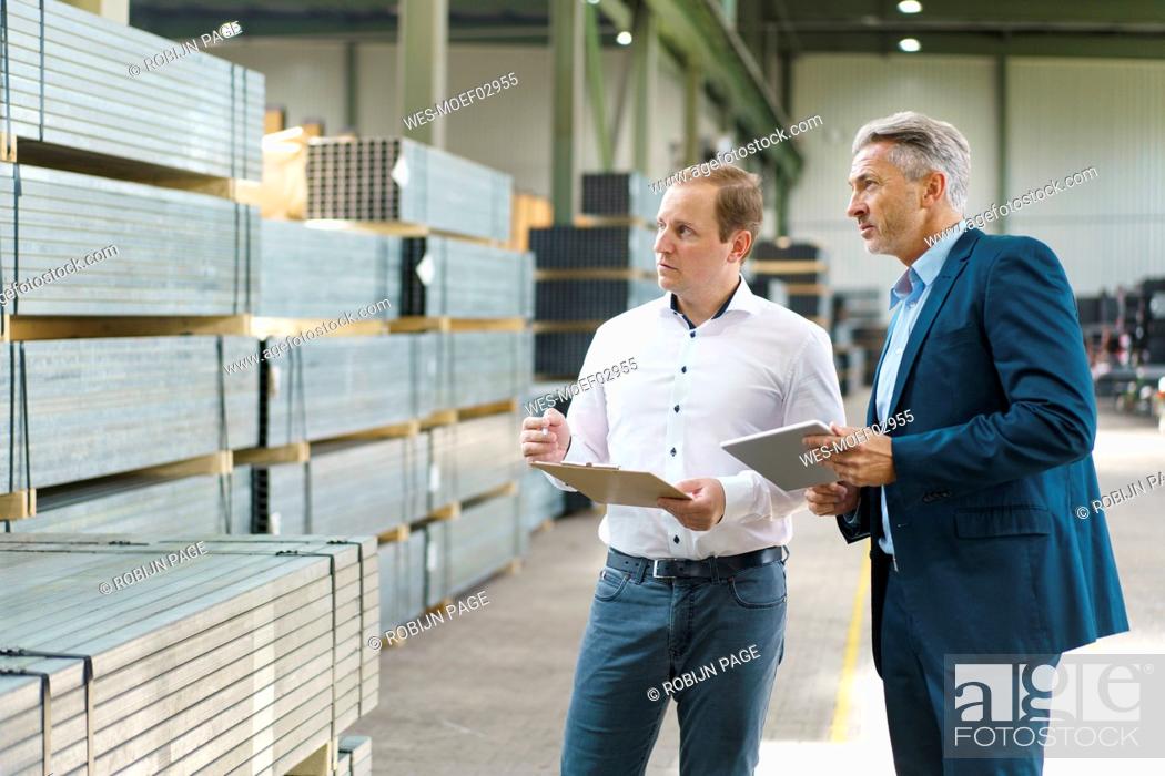 Stock Photo: Two businessmen with tablet and clipboard having a meeting in a factory.