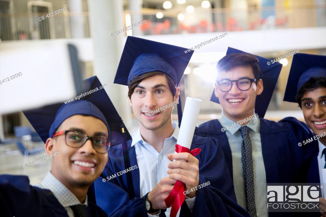Photo de stock: Male college graduates in cap and gown with diploma taking selfie.