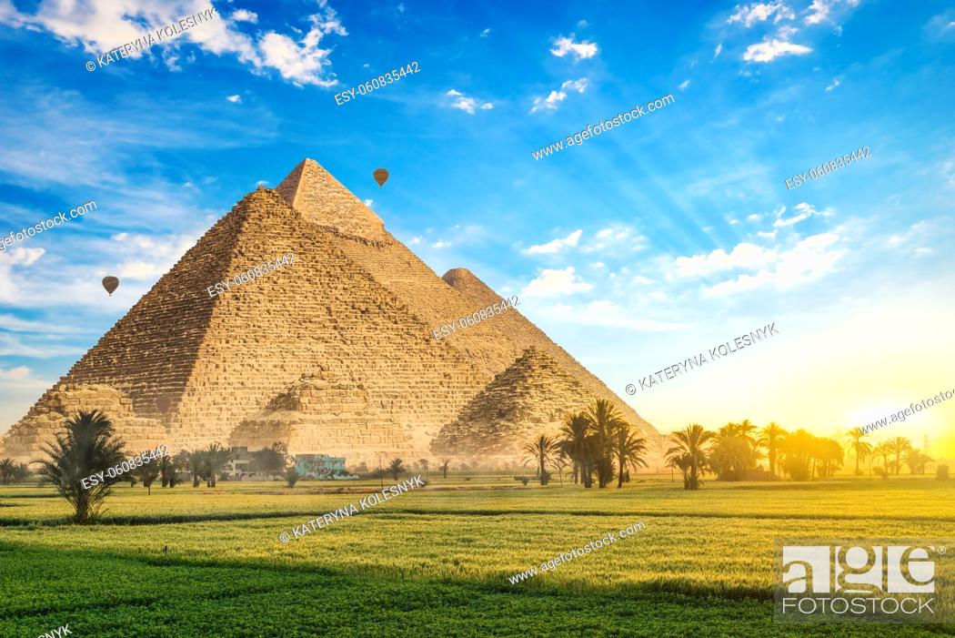 Imagen: Pyramids on green meadow with palm trees at sunrise.