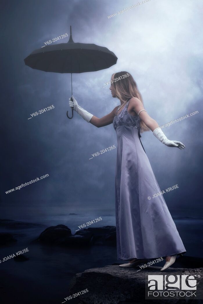 Stock Photo: a woman in a purple dress is standing at a lake with a black umbrella in the rain.