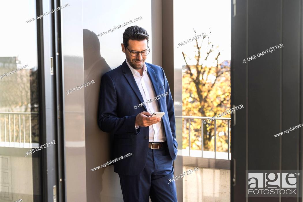 Stock Photo: Male entrepreneur using mobile phone while standing with hand in pocket by balcony at office.