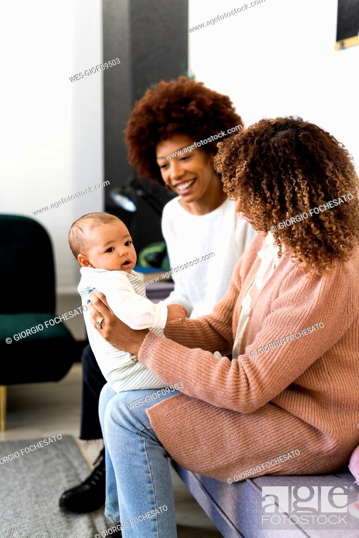 Stock Photo: Mother taking daughter on lap while aunt sitting beside on sofa at home.