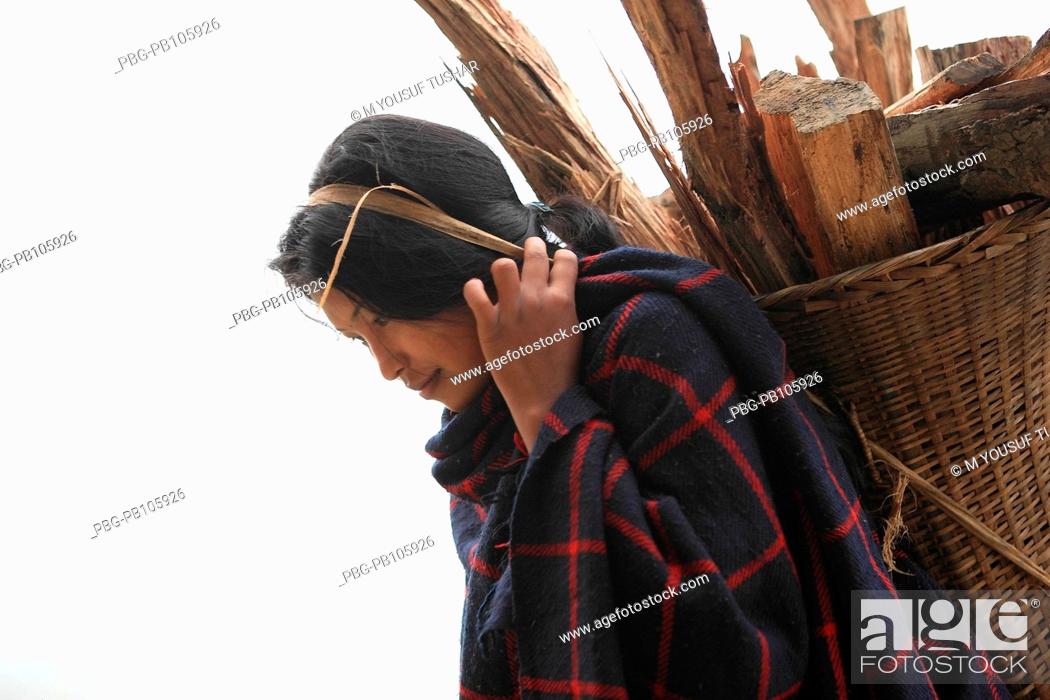 Stock Photo: An ethnic Marma woman carries basket of firewood on her back at the bank of Sangu river Bandarban, Bangladesh December 2009.