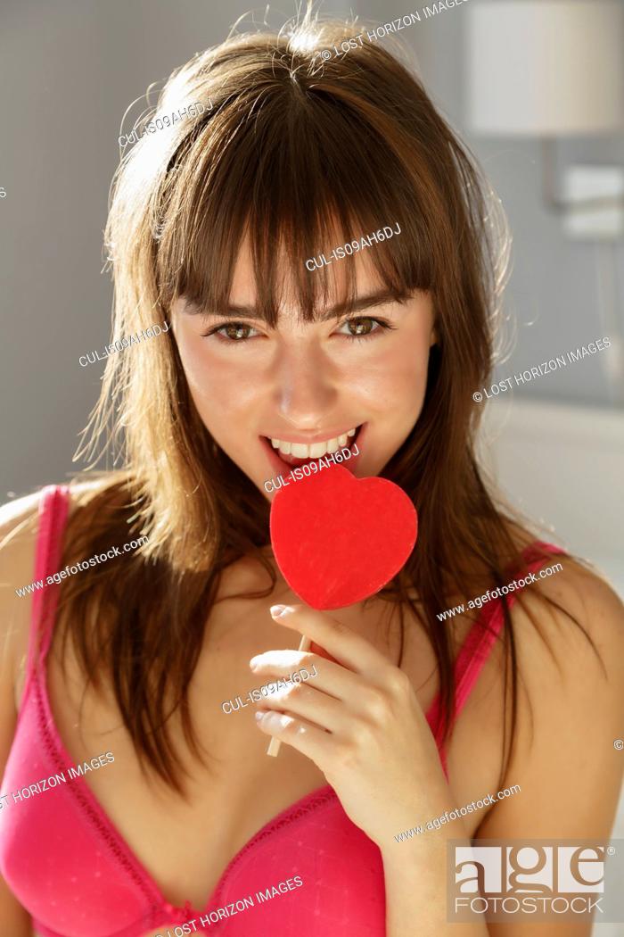 Stock Photo: Young woman biting heart shape lollipop.