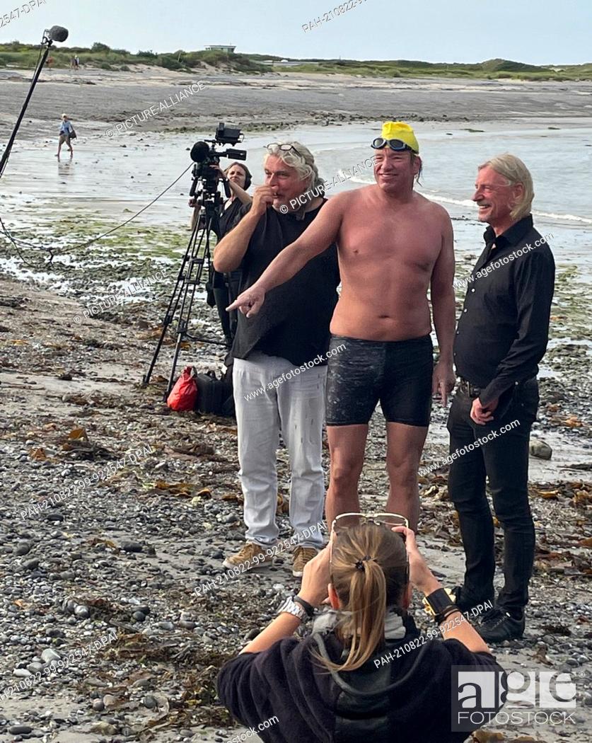 Stock Photo: HANDOUT - 21 August 2021, Schleswig-Holstein, Helgoland: Extreme swimmer Andre Wiersig (m) laughs after arriving ashore in the pig bay of the Helgoland dune.