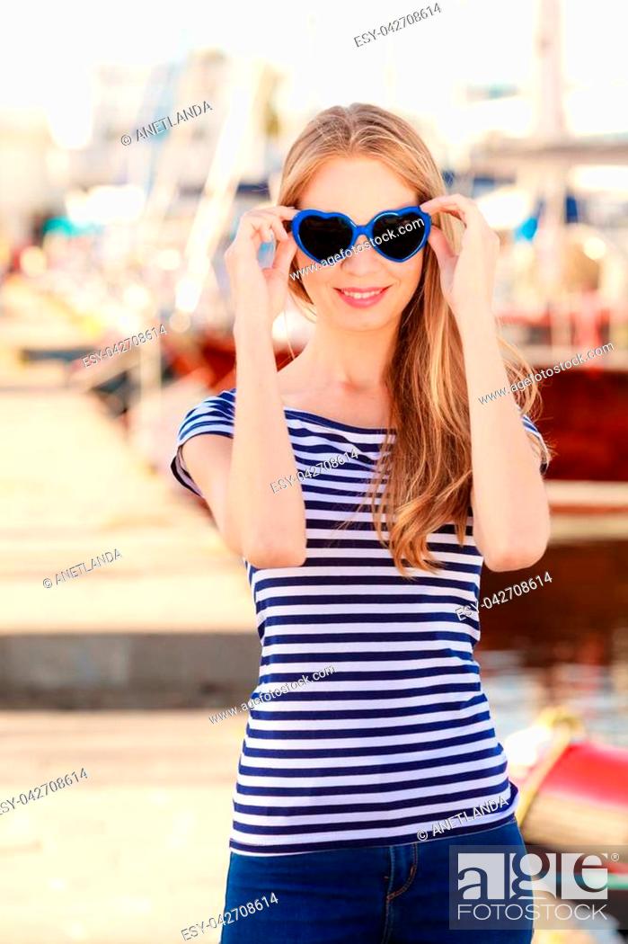 Stock Photo: Travel tourism and people concept. Fashion blonde girl with blue heart shaped sunglasses in marina against yachts in port.