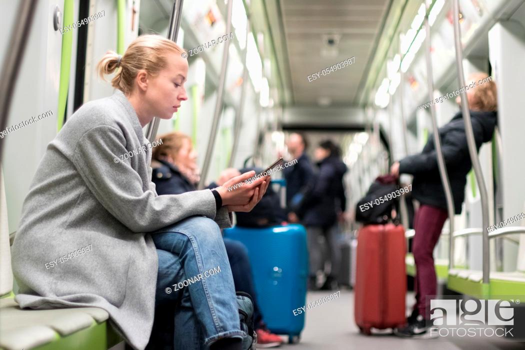 Stock Photo: Beautiful blonde caucasian woman wearing winter coat reading on the phone while traveling by metro. Public transportation concept.