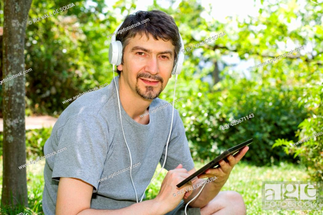 Stock Photo: young man holding a tablet with headphones, outdoor.