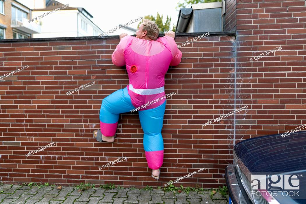 Stock Photo: Man wearing pink bodybuilder costume climbing over a wall.