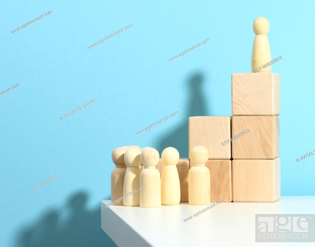 Imagen: wooden figurine of a man stands on a high podium of cubes, below the crowd. Search for talented employees, rally, manipulation of the masses.