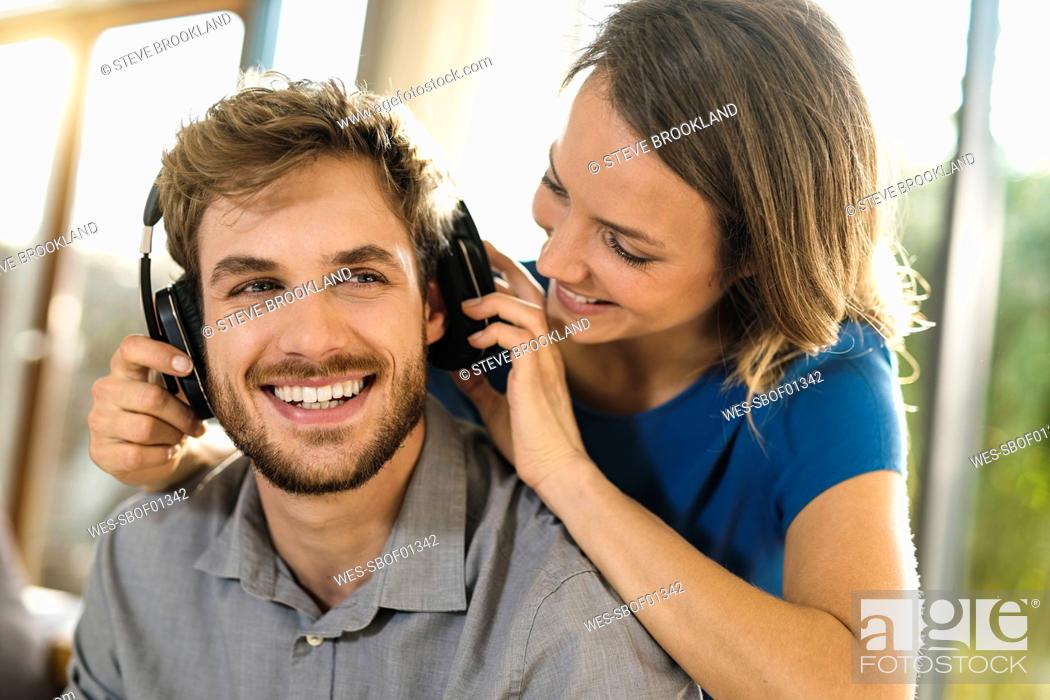 Stock Photo: Smiling woman putting on headphones on boyfriend.