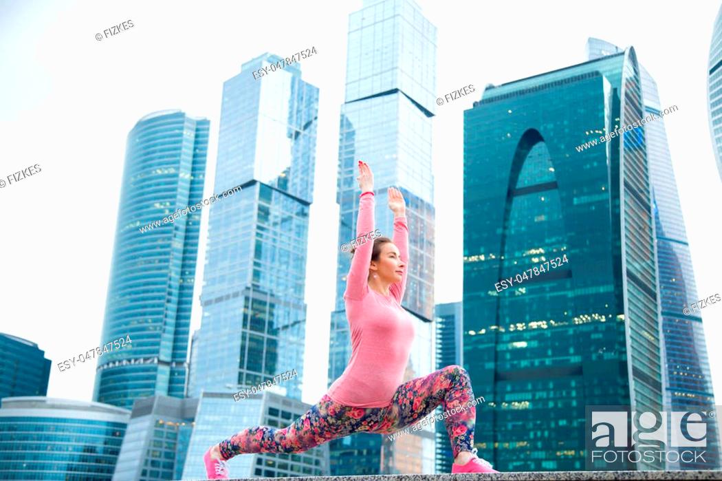 Stock Photo: Young attractive woman practicing yoga, standing in Warrior one exercise, Virabhadrasana I pose, working out wearing pink sportswear, outdoor full length.