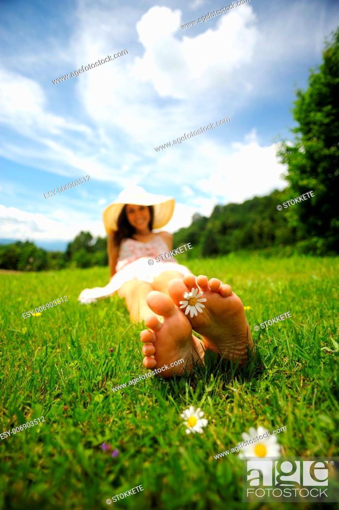 Stock Photo: a smiling young woman is lying on a green lawn, with a daisy between her toes shallow deep of field selective focus.