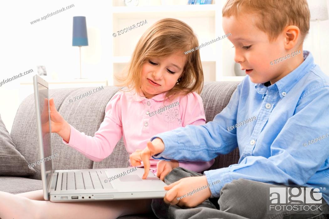 Stock Photo: Young children sitting on couch at home with laptop computer. Boy using touch pad, angry girl trying to close teh screen.
